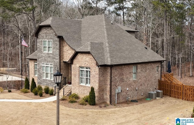 view of property exterior with central AC unit, brick siding, and roof with shingles