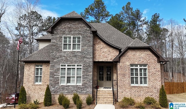 view of front of property featuring brick siding, a shingled roof, fence, french doors, and stone siding