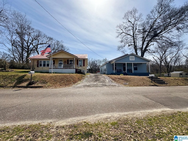 view of front of house with driveway, metal roof, and a porch