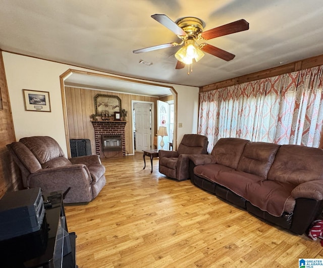 living room with a brick fireplace, visible vents, a ceiling fan, and wood finished floors