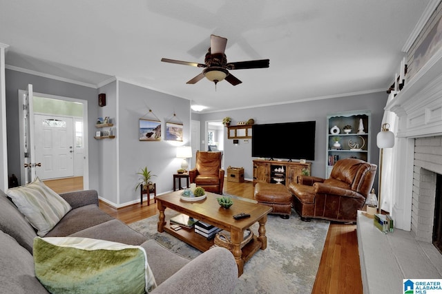 living area with crown molding, a fireplace, light wood-style flooring, ceiling fan, and baseboards