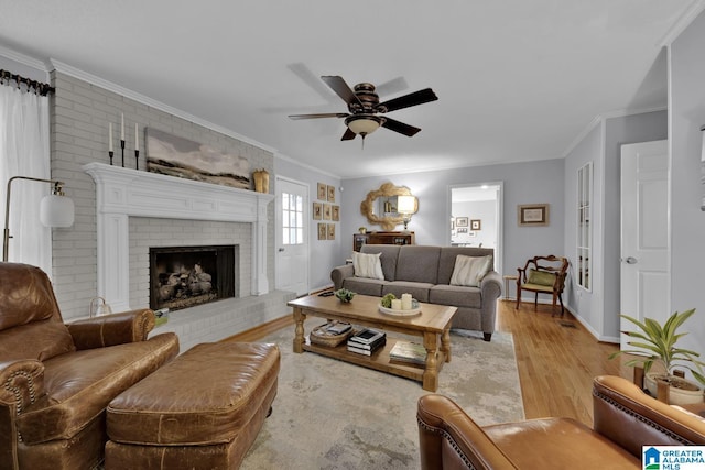 living area with baseboards, a ceiling fan, wood finished floors, crown molding, and a brick fireplace