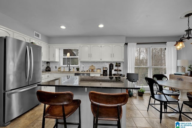 kitchen with visible vents, decorative backsplash, freestanding refrigerator, white cabinetry, and a sink