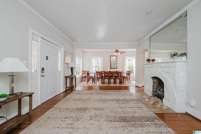 entrance foyer with a high end fireplace, ornamental molding, a ceiling fan, and wood finished floors