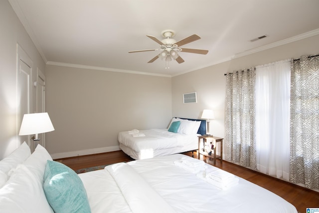 bedroom featuring visible vents, baseboards, wood finished floors, and crown molding