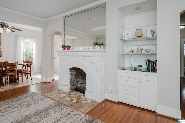 living room featuring crown molding, baseboards, hardwood / wood-style flooring, arched walkways, and a ceiling fan