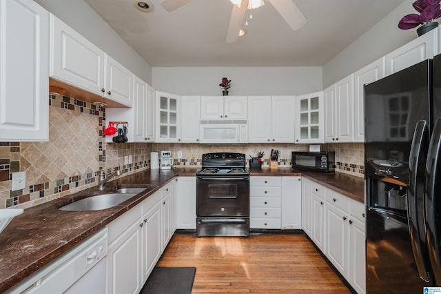 kitchen featuring a sink, decorative backsplash, black appliances, glass insert cabinets, and light wood-type flooring