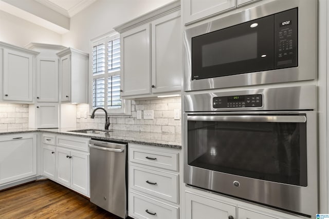 kitchen featuring white cabinets, decorative backsplash, stainless steel appliances, crown molding, and a sink