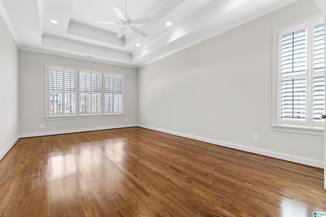 unfurnished room featuring a tray ceiling, crown molding, ceiling fan, wood finished floors, and baseboards