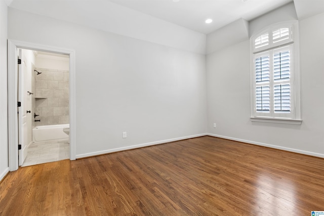 unfurnished bedroom with ensuite bathroom, recessed lighting, wood finished floors, and baseboards