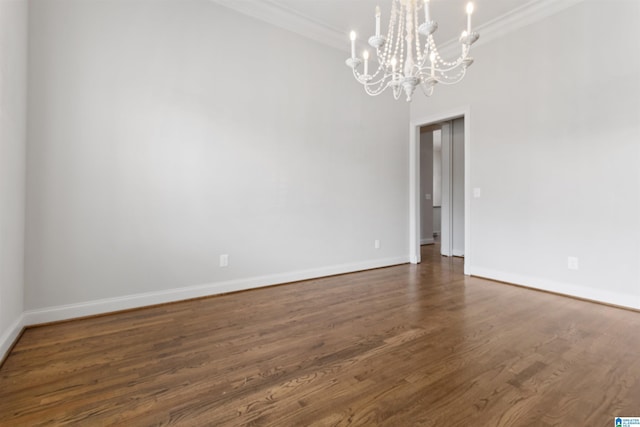 spare room featuring dark wood-style floors, ornamental molding, a chandelier, and baseboards