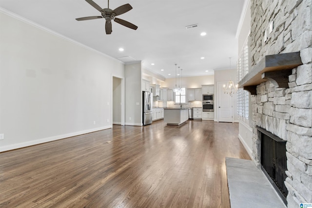 unfurnished living room with visible vents, dark wood-type flooring, ornamental molding, a stone fireplace, and baseboards