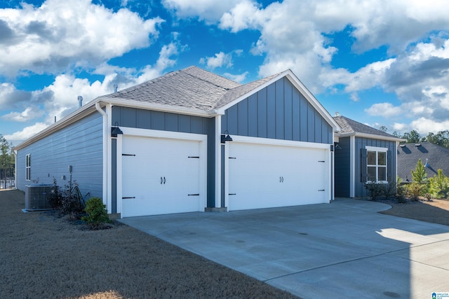 view of side of property featuring board and batten siding, concrete driveway, roof with shingles, a garage, and central AC unit