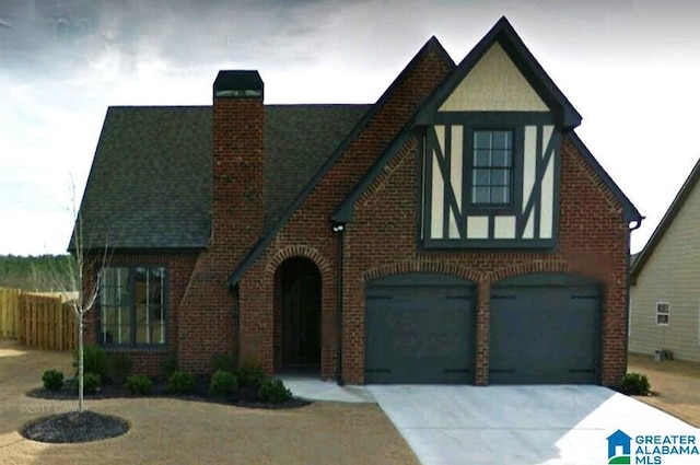 tudor home with a shingled roof, a chimney, concrete driveway, a garage, and brick siding