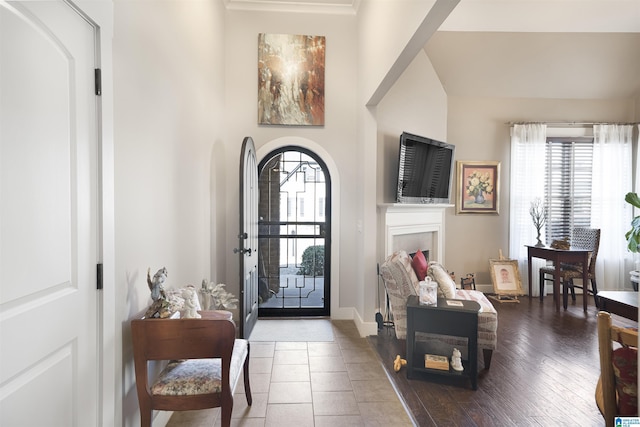 foyer featuring arched walkways, a fireplace, baseboards, and wood finished floors