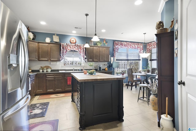 kitchen featuring visible vents, a center island, decorative light fixtures, stainless steel refrigerator with ice dispenser, and wood counters