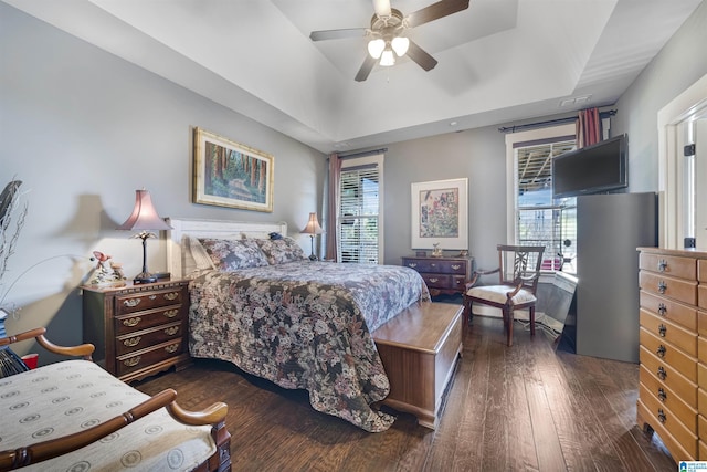 bedroom featuring a ceiling fan, a tray ceiling, and dark wood-style flooring