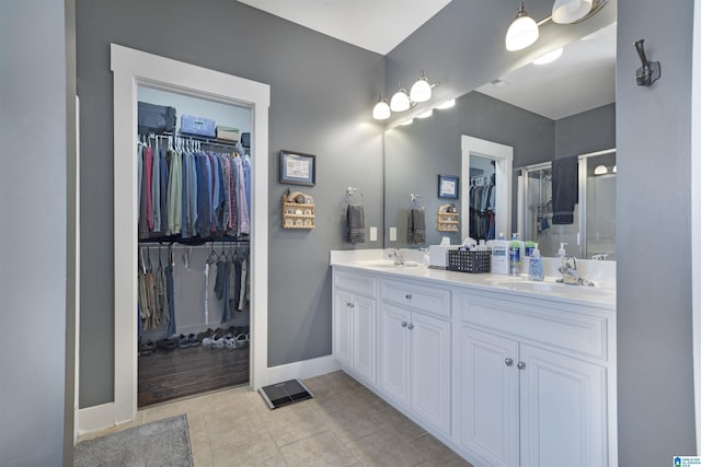 bathroom with baseboards, double vanity, a sink, a spacious closet, and tile patterned floors