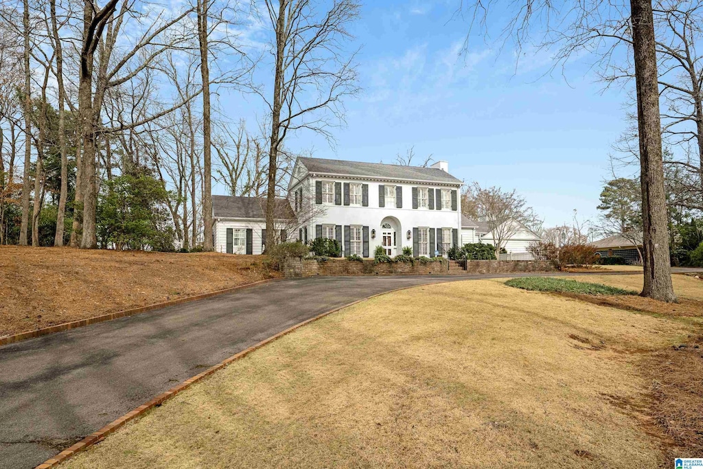 colonial house featuring driveway, a front lawn, and a chimney