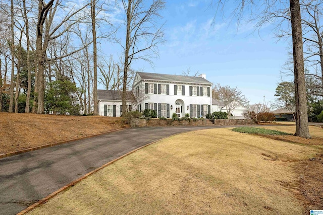 colonial house featuring driveway, a front lawn, and a chimney