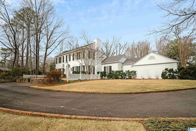 colonial-style house with a front yard, a chimney, and fence