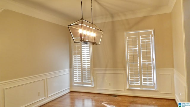 unfurnished dining area with an inviting chandelier, ornamental molding, wood finished floors, and wainscoting