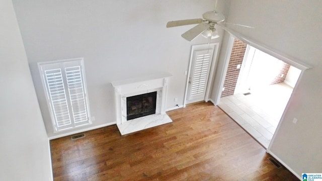 unfurnished living room featuring ceiling fan, wood finished floors, visible vents, baseboards, and a high end fireplace