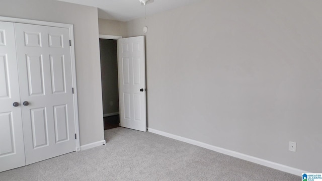 unfurnished bedroom with a closet, light colored carpet, and baseboards