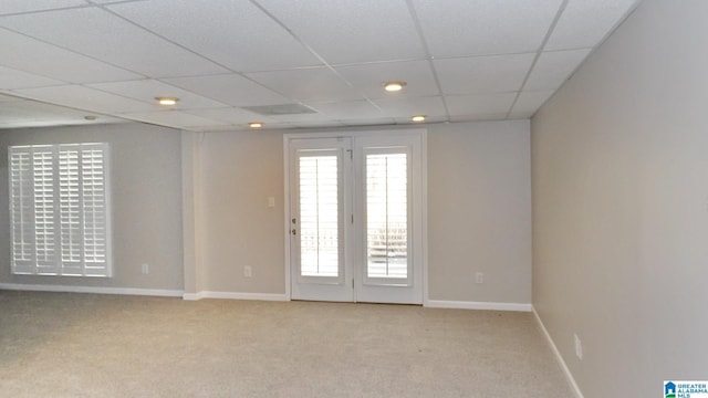 empty room featuring light carpet, a drop ceiling, and baseboards