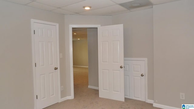 unfurnished bedroom with a paneled ceiling, light colored carpet, and baseboards