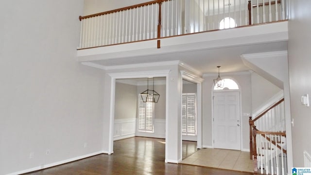 entrance foyer featuring wood finished floors, a towering ceiling, baseboards, stairway, and crown molding