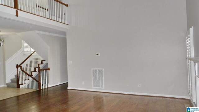 unfurnished living room with visible vents, a high ceiling, wood finished floors, baseboards, and stairs