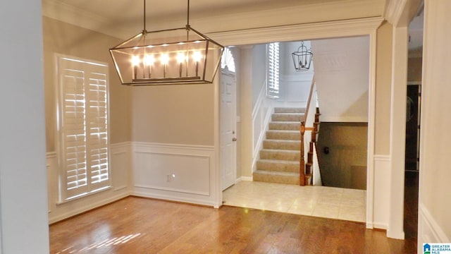 unfurnished dining area with a wainscoted wall, stairway, ornamental molding, wood finished floors, and a decorative wall