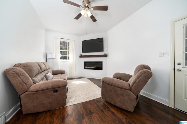 living area with ceiling fan, a glass covered fireplace, wood finished floors, and baseboards