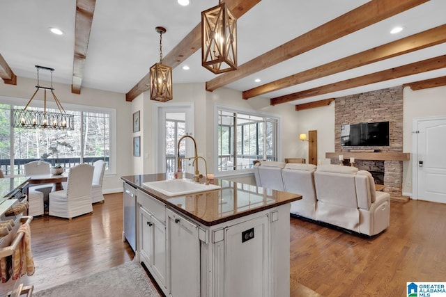 kitchen with dark countertops, open floor plan, a sink, a stone fireplace, and dishwasher