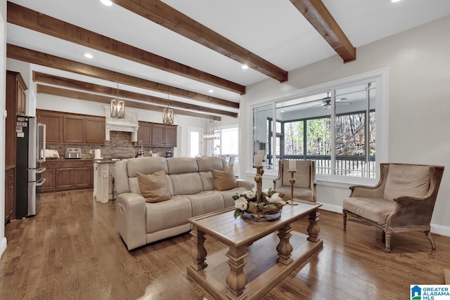 living room with beam ceiling, recessed lighting, wood finished floors, baseboards, and ceiling fan with notable chandelier