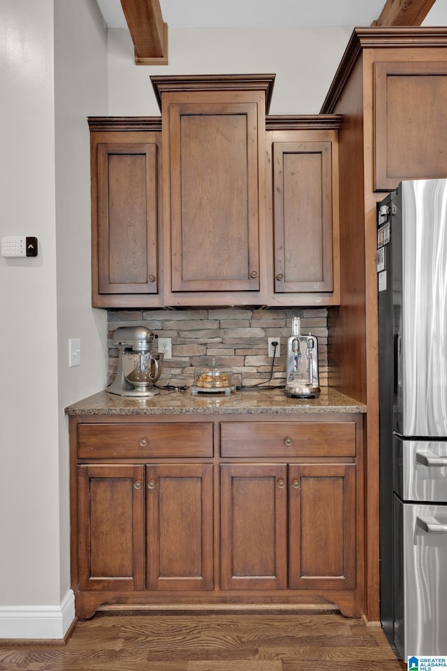 bar featuring freestanding refrigerator, backsplash, baseboards, and wood finished floors