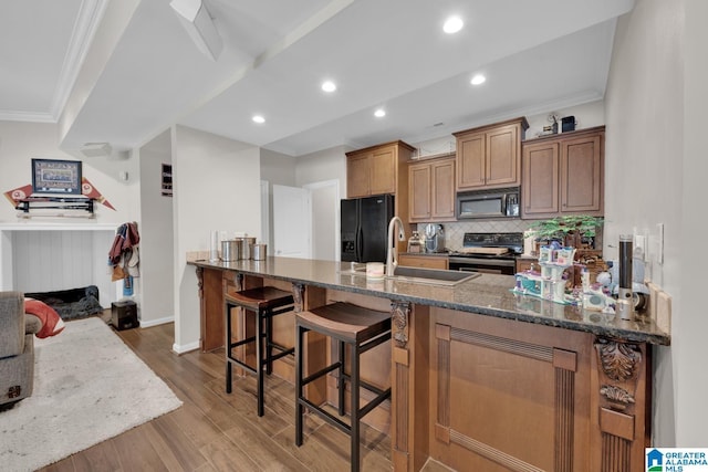 kitchen featuring ornamental molding, dark stone countertops, wood finished floors, a peninsula, and black appliances