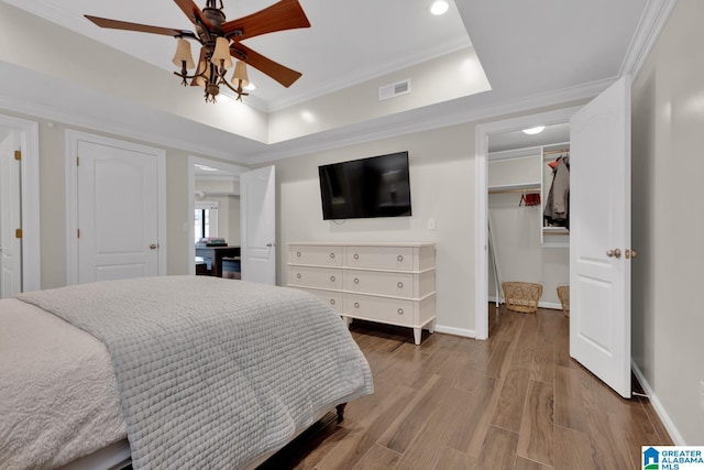 bedroom featuring visible vents, wood finished floors, a spacious closet, a tray ceiling, and crown molding