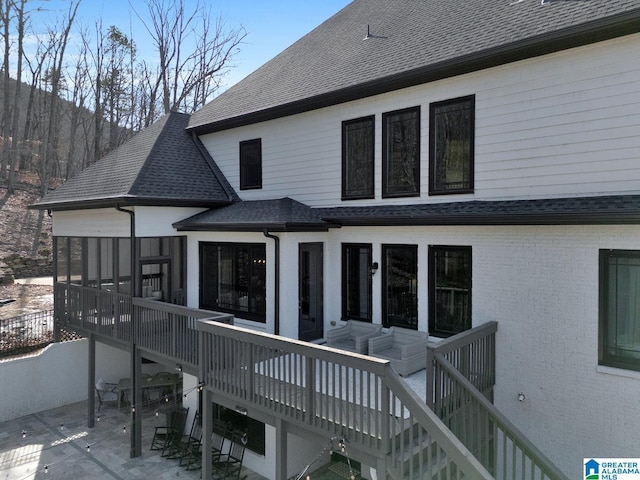 rear view of house featuring a shingled roof, brick siding, a sunroom, stairway, and a patio area