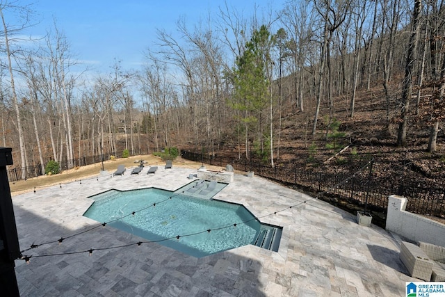 view of pool with a fenced in pool, a patio area, fence, and a forest view