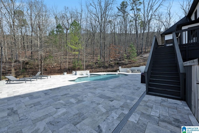 view of swimming pool with a fenced in pool, stairs, a wooded view, and a patio