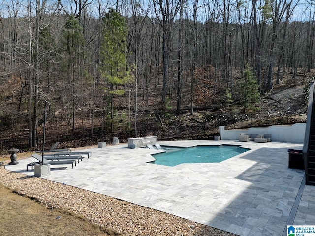 outdoor pool with a patio, an outdoor living space, and a view of trees