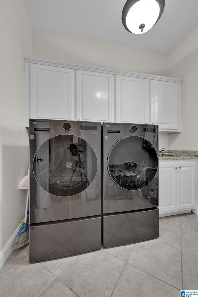 laundry area featuring light tile patterned flooring, independent washer and dryer, cabinet space, and baseboards