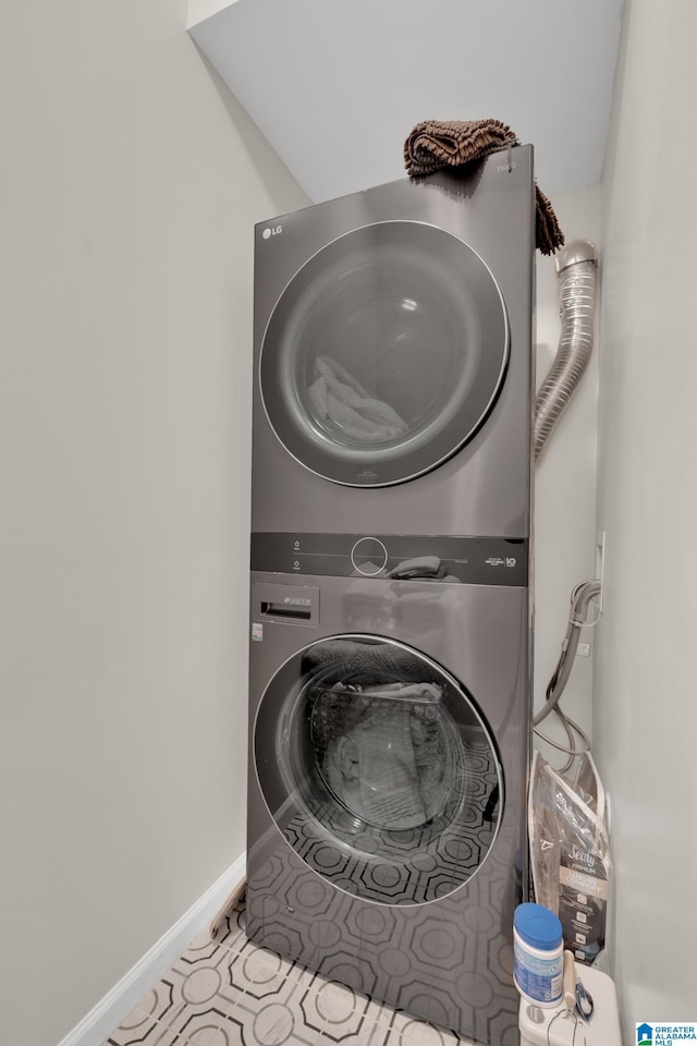 clothes washing area featuring tile patterned flooring, laundry area, baseboards, and stacked washing maching and dryer