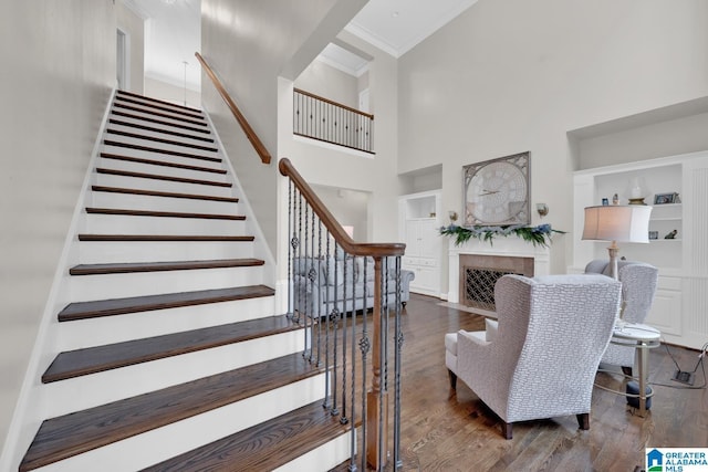 staircase with a fireplace with flush hearth, ornamental molding, a high ceiling, and wood finished floors