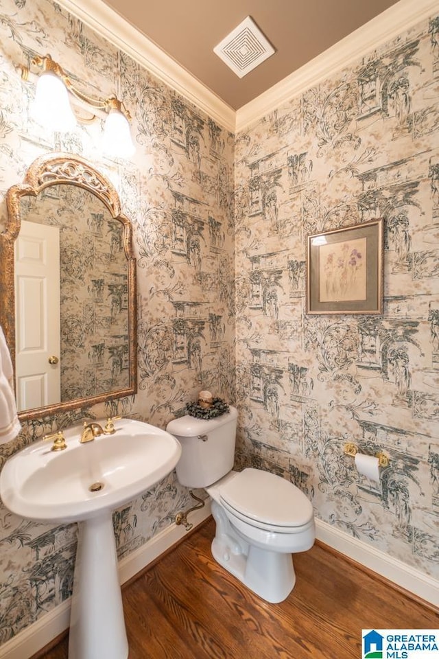 bathroom with toilet, wood finished floors, visible vents, baseboards, and crown molding