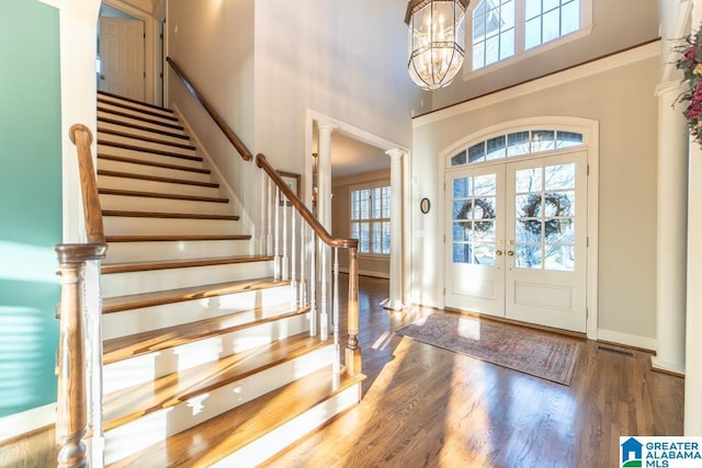 foyer with french doors, stairway, a towering ceiling, wood finished floors, and ornate columns