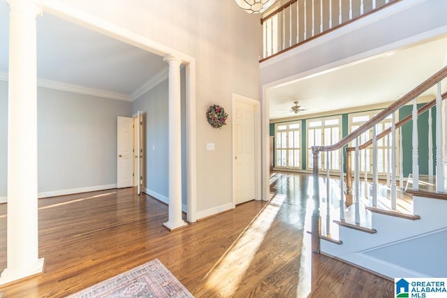 entryway featuring baseboards, wood finished floors, decorative columns, and crown molding