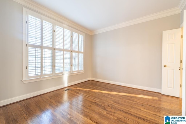 spare room with baseboards, visible vents, crown molding, and wood finished floors